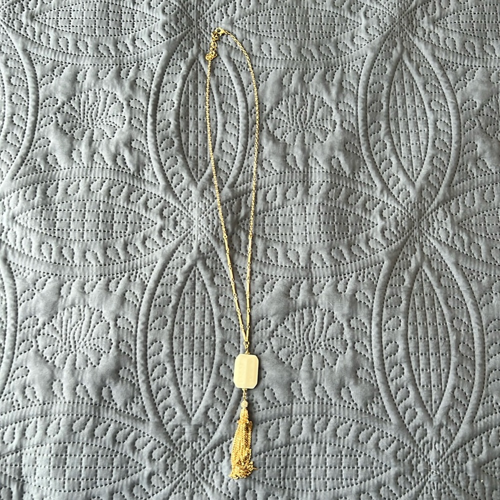 Long gold-color necklace with white pendant.